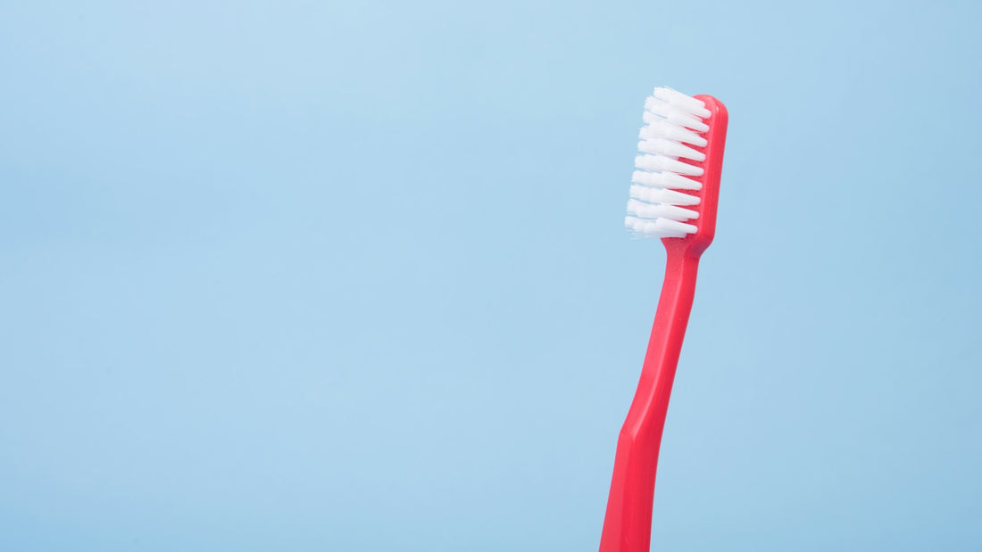 Brosse à dents manuelle rouge sur fond bleu, illustration générique d’une routine de brossage.